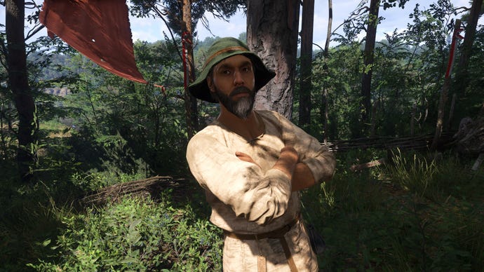 A close-up of Horse Handler Mikolai, an NPC in Kingdom Come: Deliverance 2, leaning against a tree in a Nomad Camp with his arms folded, looking at the camera.