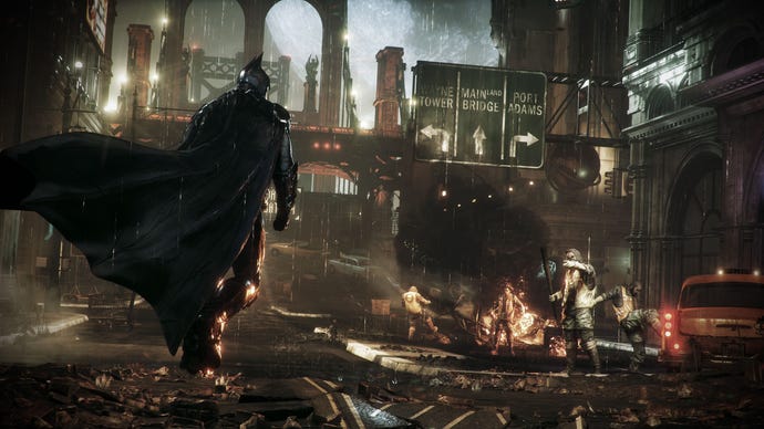 Batman walks in ruined city streets with his cape falpping as looters burn cars in the background.